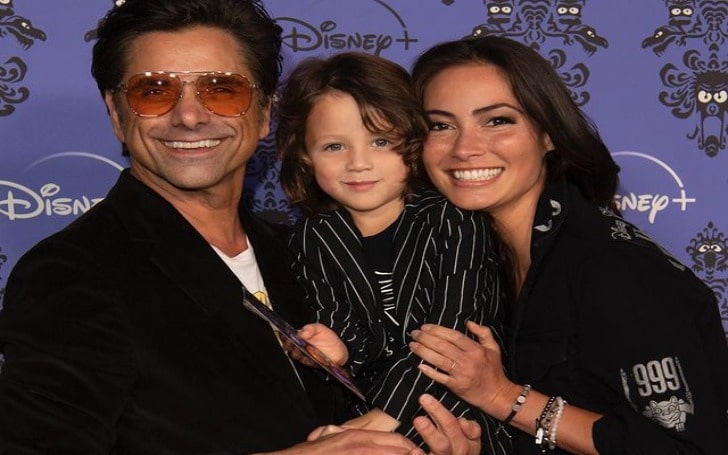 Billy Stamos smiling is a black suit with white lines in his parents' arms.